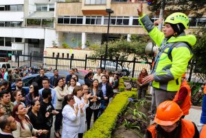 a la derecha una persona dando indicaciones de seguridad y a la izquierda una multitud de personas